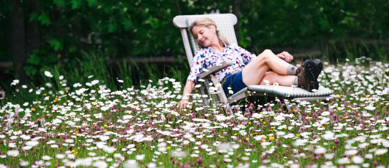 Dame liegt am Liegestuhl in einer Blumenwiese