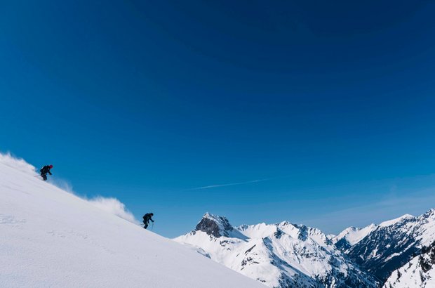 Zwei Skifahrer fahren einen verschneiten Hang hinunter