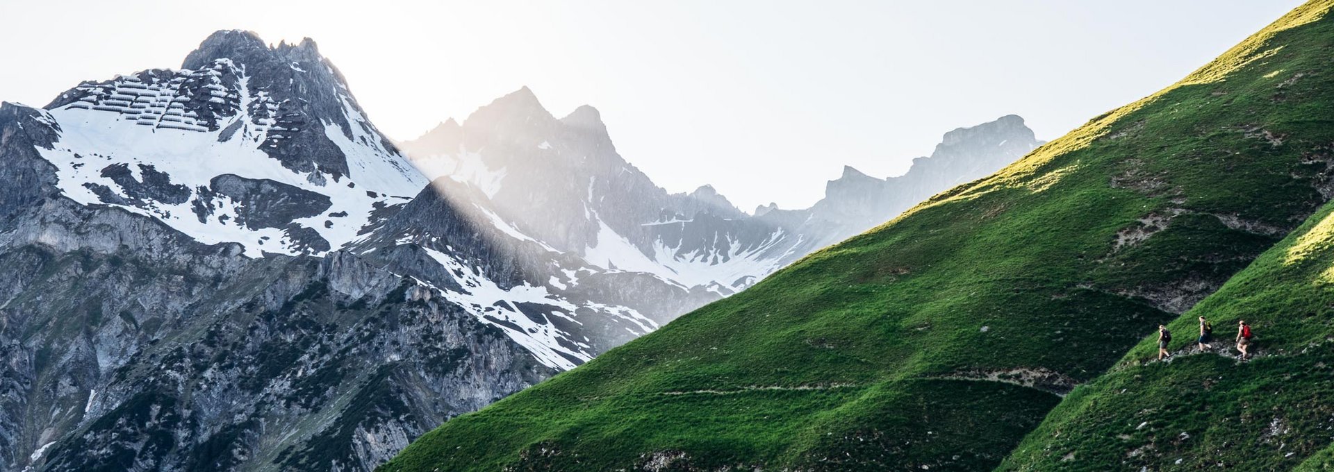Lech Wanderung Drei Personen wandern an einem schmalen Pfad entlang mit Ausblick auf die schroffen Gipfel.